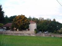                 
    Vue de l'école, au premier plan, un pré, au fond l'école et le préau vitré, derrière, la forêt.                