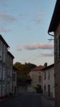           
    Vue de la rue basse, de part et d'autre de la rue les maisons s'alignent. Au bout, la rue se sépare en deux. Au fond, le ciel bleu. Des nuages rosis par le soleil couchant, flottent.        